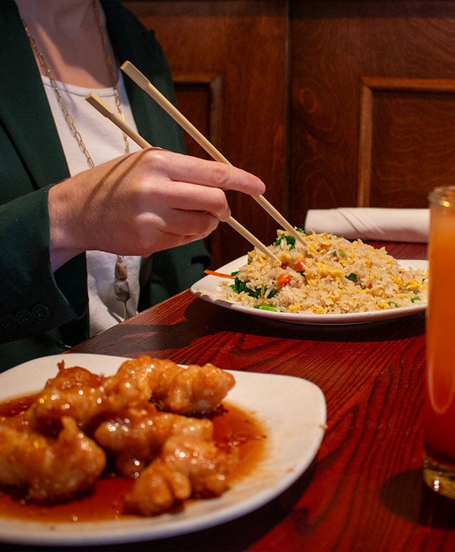 A woman uses chopsticks to eat a plate of fried rice